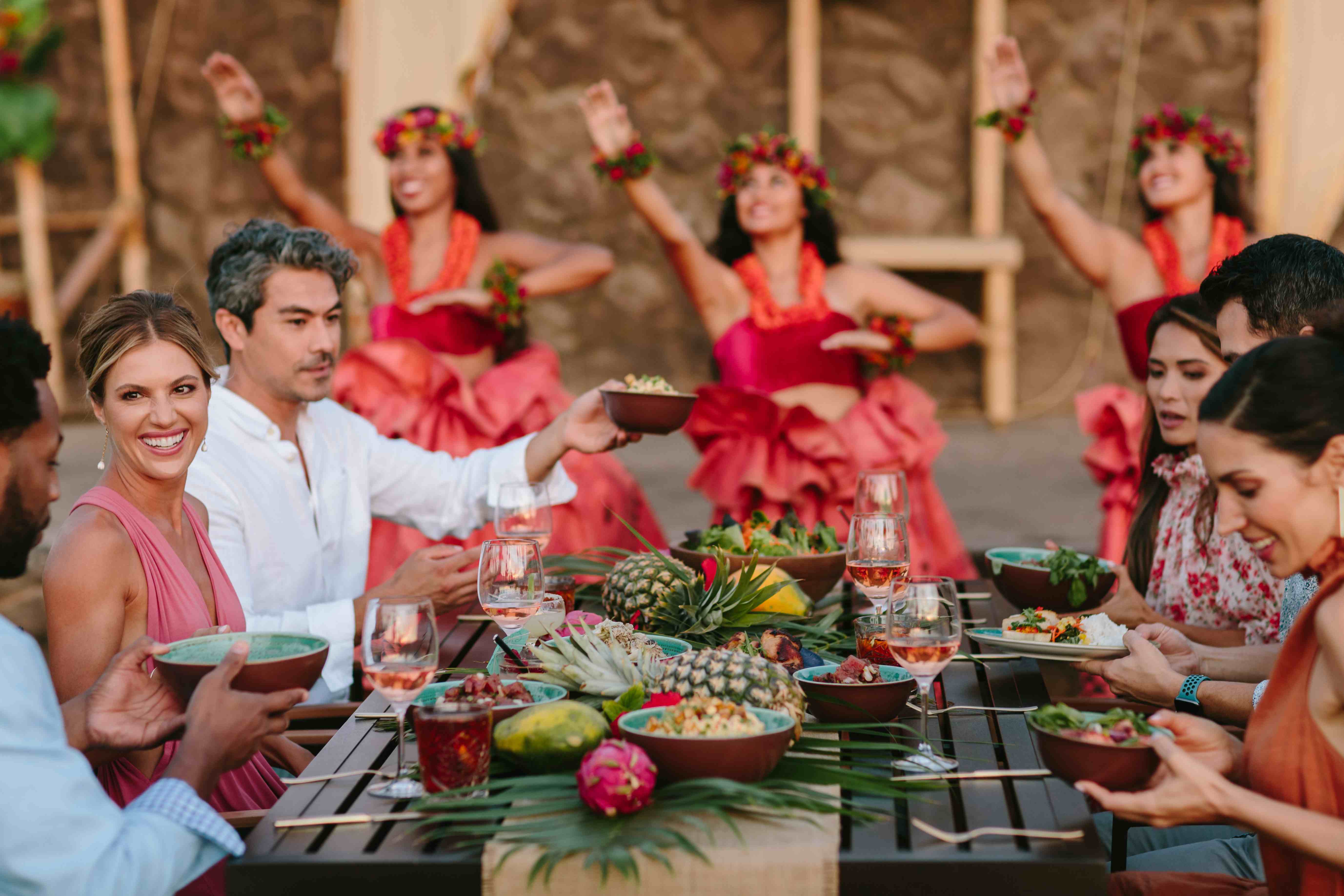 People eating at a table with hula dancers in the background